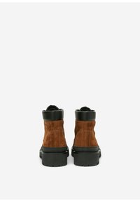 Braune Wildleder-Stiefeletten mit einer schwarzen Gummisohle und einem Kragen. Mit sichtbaren Nähten und einer strukturierten Oberfläche im Obermaterial.