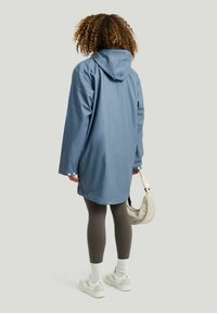 Vattentät blå anorak med huva, med en lös passform, knäppta manschetter och en mjuk yta, tillsammans med grå leggings och vita sneakers.