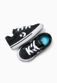 Zapatillas de lona negras con cordones blancos y suelas de goma. Presentan un logo de estrella blanca y una plantilla azul con un patrón circular.