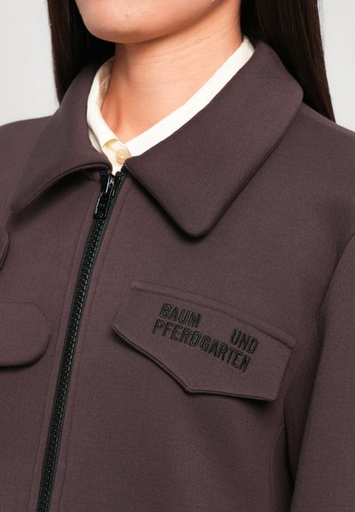 Σκούρο μωβ φερμουάρ jacket με κολάρο και δύο μπροστινές τσέπες.Το "BAUM UND PFEROGAERTEN" κομμένο με μαύρο κλωστή στην αριστερή τσέπη. Λείος υφασμάτινος υλικό.