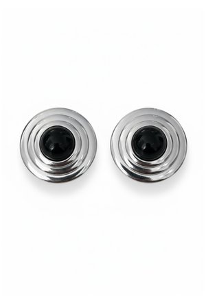 Par de pendientes redondos de plata con diseño de círculos concéntricos y una piedra negra en forma de cúpula en el centro, sobre fondo blanco.