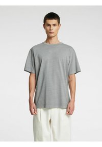 Grå oversized T-skjorte i mykt stoff, med korte ermer og rund hals, kombinert med lyse, løstsittende bukser.