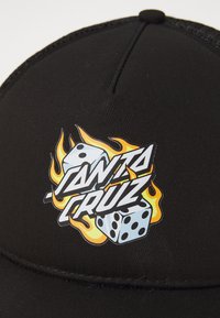 Black cap with a flat brim features a graphic logo. Design includes dice, flames, and the text "SANTA CRUZ" in bold colors.