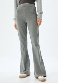 Pantalones de chándal grises acampanados hechos de una tela suave y elástica con una textura lisa. Cintura cómoda y diseño casual, combinados con zapatos blancos.