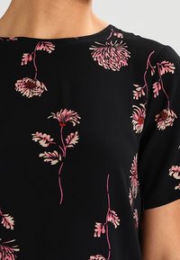Black short-sleeve top with pink and light purple floral patterns scattered across the fabric.