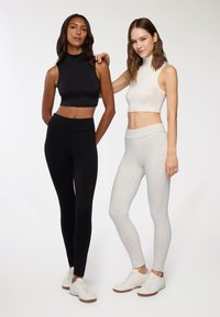 Dwie modelki noszą dopasowane topy odsłaniające brzuch i legginsy: jedna w czerni, a druga w bieli i jasnej szarości. Wszystkie ubrania są w jednolitych kolorach i bezszwowe.