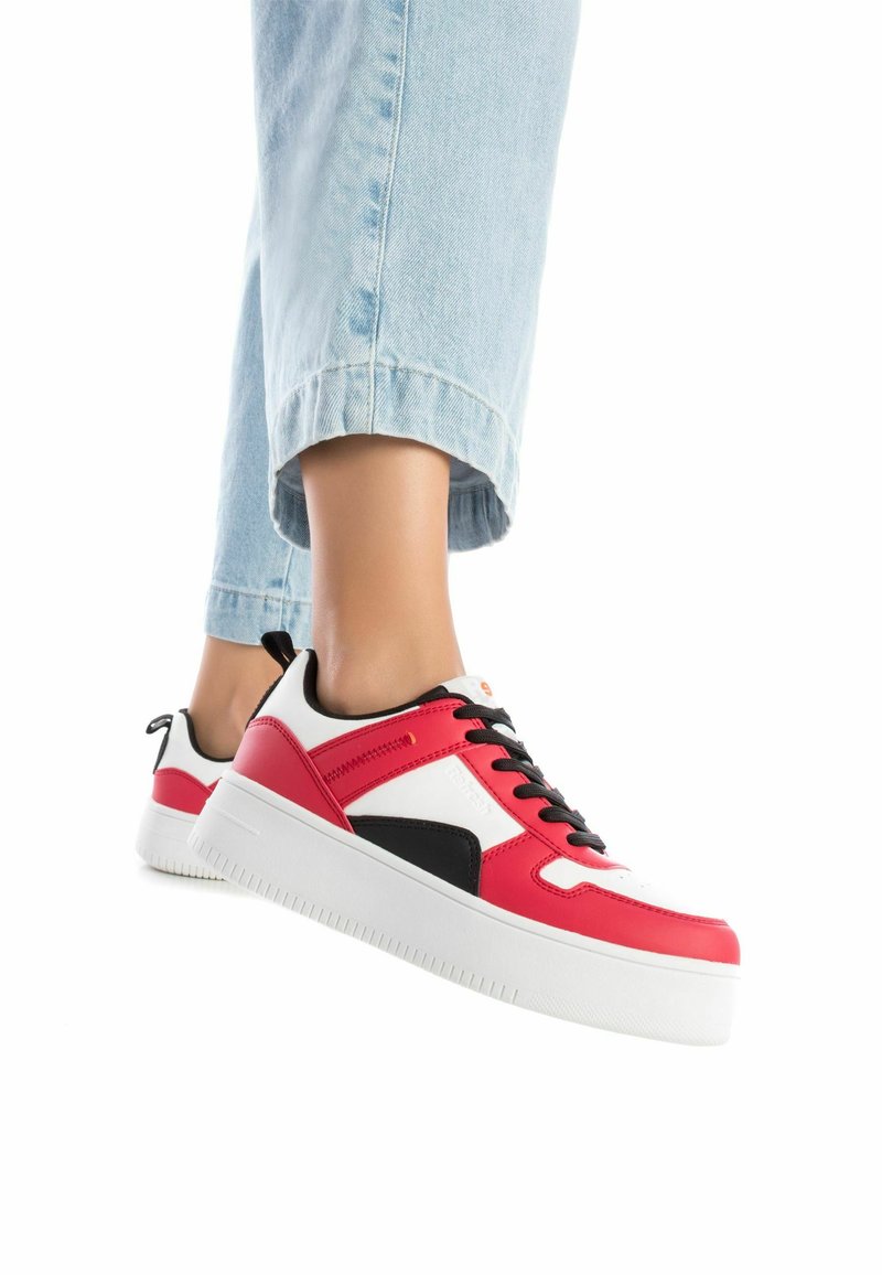 Zapatilla roja y blanca con acentos negros, parte superior de cuero y textil suave, suela blanca gruesa, con cordones negros y detalles de marca.