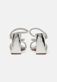 Sandali con tacco a blocco argentati, decorati con strass e sottili cinturini. Superficie metallizzata liscia con una soletta opaca e suola testurizzata.