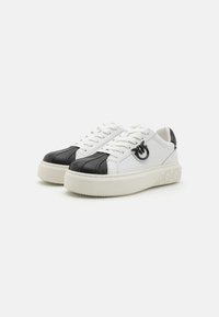 White and black leather sneakers with a thick white sole, featuring textured black toe and a logo accent on the side.