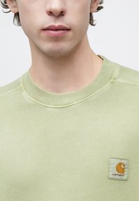 Ανοιχτό πράσινο φούτερ με ριμπ λαιμόκοψη και τετράγωνο λογότυπο Carhartt σε πορτοκαλί και λευκό στο αριστερό στήθος.