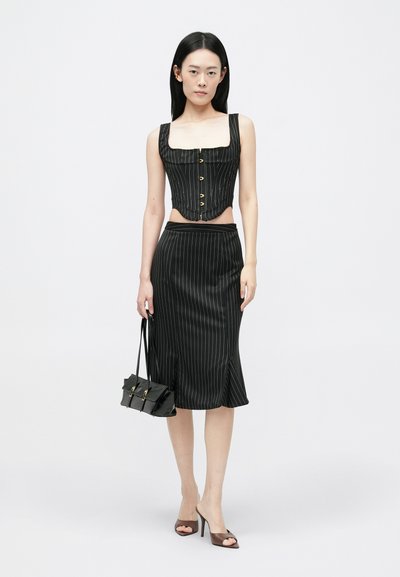 Top de corsé negro a rayas con escote cuadrado y botones, combinado con una falda lápiz a juego. El modelo sostiene un pequeño bolso negro.