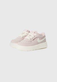 Sneakers Nike con una toma superiore sintetica di colore rosa chiaro, lacci bianchi e una suola in gomma testurizzata, con un logo discreto sul lato.