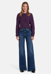 Pullover viola con texture e motivo ondulato, abbinato a jeans a vita alta a campana blu e scarpe nere. Un outfit semplice e informale.
