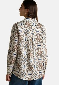 Long-sleeve shirt in light fabric, featuring an intricate pattern of ropes and hardware in brown, green, and blue on a cream background.
