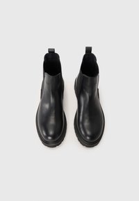 Bottines en cuir noir avec une texture lisse, des panneaux latéraux élastiques et une semelle en caoutchouc épaisse. Équipées de languettes pour un enfilage facile.