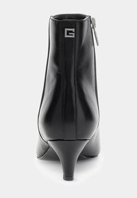 Stivaletti alla caviglia in pelle nera con punta appuntita, tacco sottile e cerniera laterale. Presentano un dettaglio logo metallico sul retro. Texture liscia.