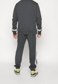 Dark gray sweatshirt and matching joggers, both in a soft material, featuring white side stripes and ribbed cuffs. Sneakers with visible cushioning.