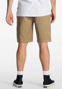 Pantaloni shorts color khaki realizzati in cotone, con taglio dritto, tasche laterali e orli cuciti, abbinati a sneaker alte nere.