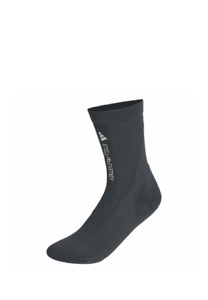 Schwarze Socke bis zur Mitte der Wade mit weißem "Stella McCartney"-Schriftzug und Adidas-Logo, die vertikal an der Seite aufgedruckt sind.