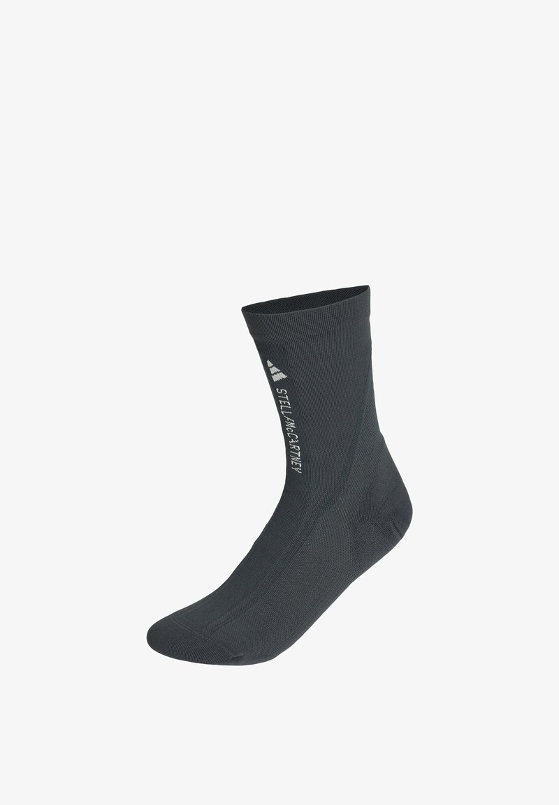 Schwarze Socke bis zur Mitte der Wade mit weißem "Stella McCartney"-Schriftzug und Adidas-Logo, die vertikal an der Seite aufgedruckt sind.