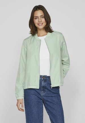 Mint green bomber jacket with elastic cuffs and waistband, zip closure, worn over a white top, paired with blue high-waisted jeans.