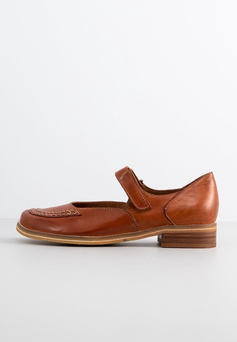 Chaussure Mary Jane en cuir marron avec détails cousus, talon bas empilé et bride ajustable sur fond neutre.