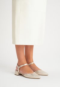 Sandały na obcasie z noskiem w kształcie szpica, metaliczne, złote, z niskim słupkiem i paskiem wokół kostki. Gładka tekstura z delikatnym połyskiem.