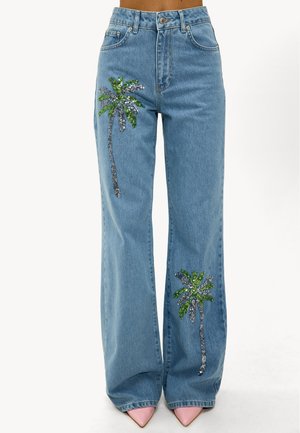 Vaqueros de mezclilla azul claro con perneras anchas que presentan diseños de palmeras en lentejuelas verdes y plateadas en cada pierna delantera. La forma es relajada y casual.