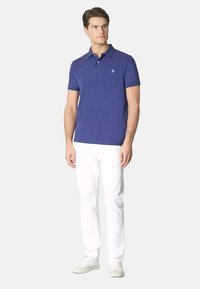 Polo azzurro con colletto e maniche corte, con un piccolo logo sul petto. Abbinato a pantaloni bianchi e sneaker di colore chiaro.