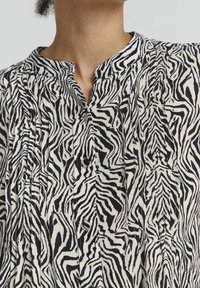 Blusa a stampa zebraccia con motivi in bianco e nero, chiusura con bottoni e colletto alla cinese, realizzata in tessuto leggero con pieghe.
