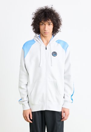 Haut de sweatshirt zippé gris clair avec des accents bleus et le logo Nike. Fabriqué en tissu doux, il comprend une capuche, des poches kangourou et une texture lisse.