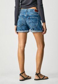 Siniset farkkushortsit, joissa on käännetyt lahkeet, takataskut ja nahkainen merkki. Yhdistetty mustiin niitattuihin sandaaleihin, paljain jaloin.