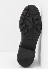 Semelle de chaussure en caoutchouc noir avec un motif de bande de roulement profond, des zones d'adhérence texturées et le logo Emporio Armani près du talon et au centre.