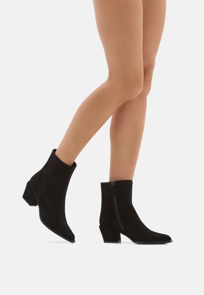 Stivaletti neri in suede fino alla caviglia con punta affusolata, tacco a blocco di 3 cm e dettagli con zip laterale. Texture liscia con un design pulito.