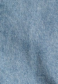 Ljusblå denimtyg med ett synligt twill-vävmönster. Mjuk textur med subtila variationer i färg och fibrer över ytan.