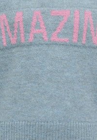 Svetlo modra pletena majica z besedo "AMAZING" v nežno roza barvi, z rebrastim robom in gladko teksturo povsod.