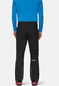 Sorte udendørsbukser har en lige pasform, forstærkede nederste ben og lynlåslommer. Kombineret med rødt fodtøj og en blå langærmet top.