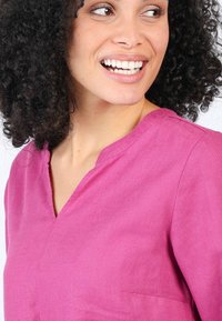 Rosa Leinenhemd mit V-Ausschnitt und kurzen Ärmeln, das eine strukturierte Oberfläche und eine kleine Tasche auf der linken Vorderseite aufweist.