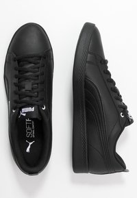 Zapatillas de cuero negro con suelas planas, punteras redondas, cuellos acolchados y acentos blancos contrastantes. Presentan cordones y un panel lateral texturizado.