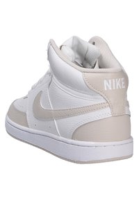 Sneakers Nike alta in pelle bianca con accenti beige. Presentano una superficie texture, un collare imbottito e un logo sul tallone.