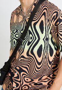 Chemise à manches courtes arborant un motif abstrait vibrant dans des nuances de pêche, noir et vert. Fabriquée en tissu léger avec une coupe ample.
