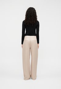 Pantalon beige à jambes larges avec une texture lisse, doté de deux poches arrière et d'une taille haute, assorti à un haut noir à manches longues.