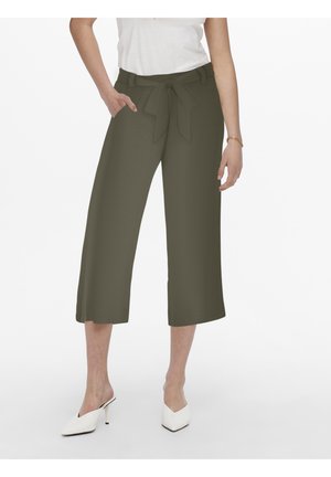 Mujer con pantalones anchos cortos de color verde oliva con lazo en el cinturón, top blanco y mules blancos de tacón con punta afilada.