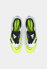 Une paire de crampons de football Adidas Predator blancs et vert fluo avec des bandes velcro noires et le texte "PREDATOR" sur les semelles intérieures.