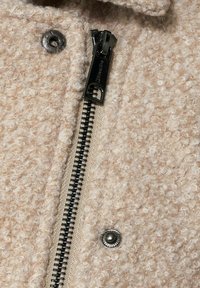 Beige texturovaná vlněná bunda s černým kovovým zipem, se zapínáním na cvok a tkaninovým detailem podél zipu.