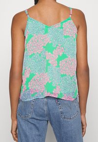 Bez rękawów, lekka bluzka w kolorze zielonym z kwiatowym wzorem w różu i błękicie. V-kształtny tył, cienkie ramiączka i luźny krój.