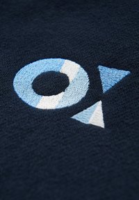 Tessuto navy con forme circolari e triangolari ricamate in azzurro chiaro e bianco. La finitura testurizzata esalta i dettagli visivi.