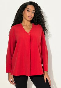 Blusa rossa a maniche lunghe con scollo a V e dettaglio di un singolo bottone, realizzata in tessuto morbido, con una vestibilità ampia e un design plissettato sul davanti.