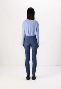 Světle modrá košile s dlouhými rukávy v kombinaci s tmavě modrými slim džíny. Džíny mají standardní pas a zadní kapsy. Viditelné černé boty.