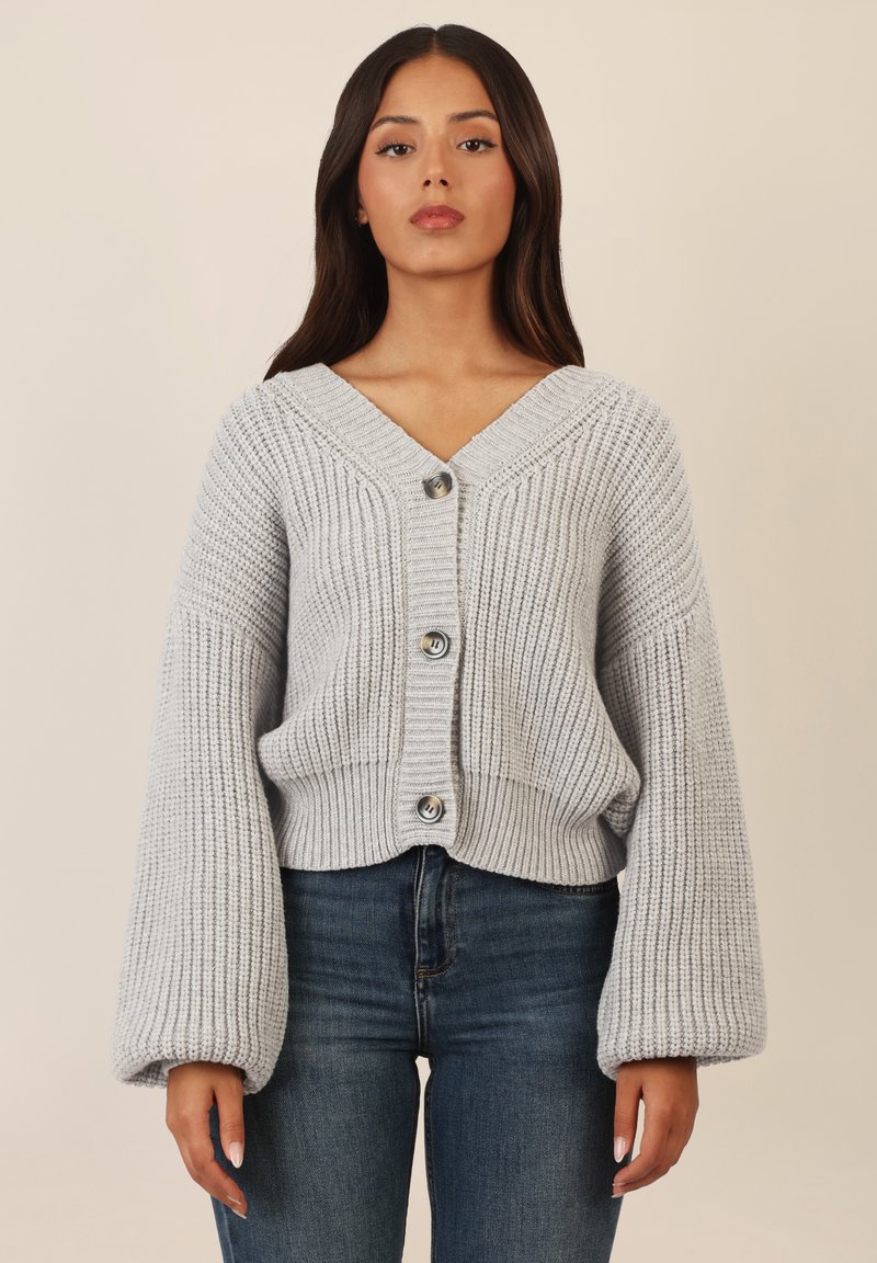 Cardigan grigio a maglia con scollo a V, maniche oversize e tre bottoni anteriori. Tessuto testurizzato e design corto.